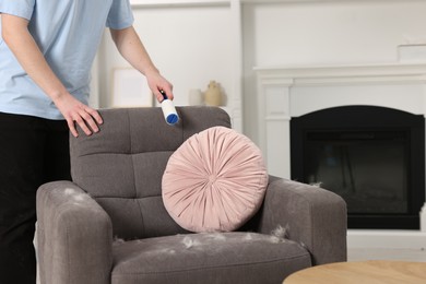 Photo of Pet shedding. Man with lint roller removing dog's hair from armchair at home, closeup