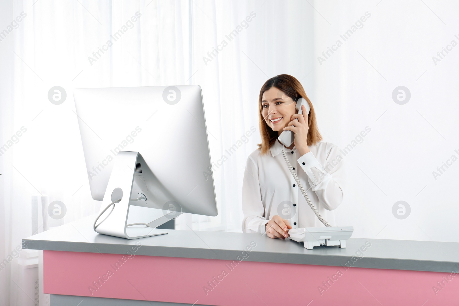 Photo of Beautiful woman talking on phone at reception desk in beauty salon