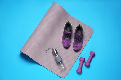 Photo of Exercise mat, dumbbells, bottlewater and shoes on turquoise background, flat lay