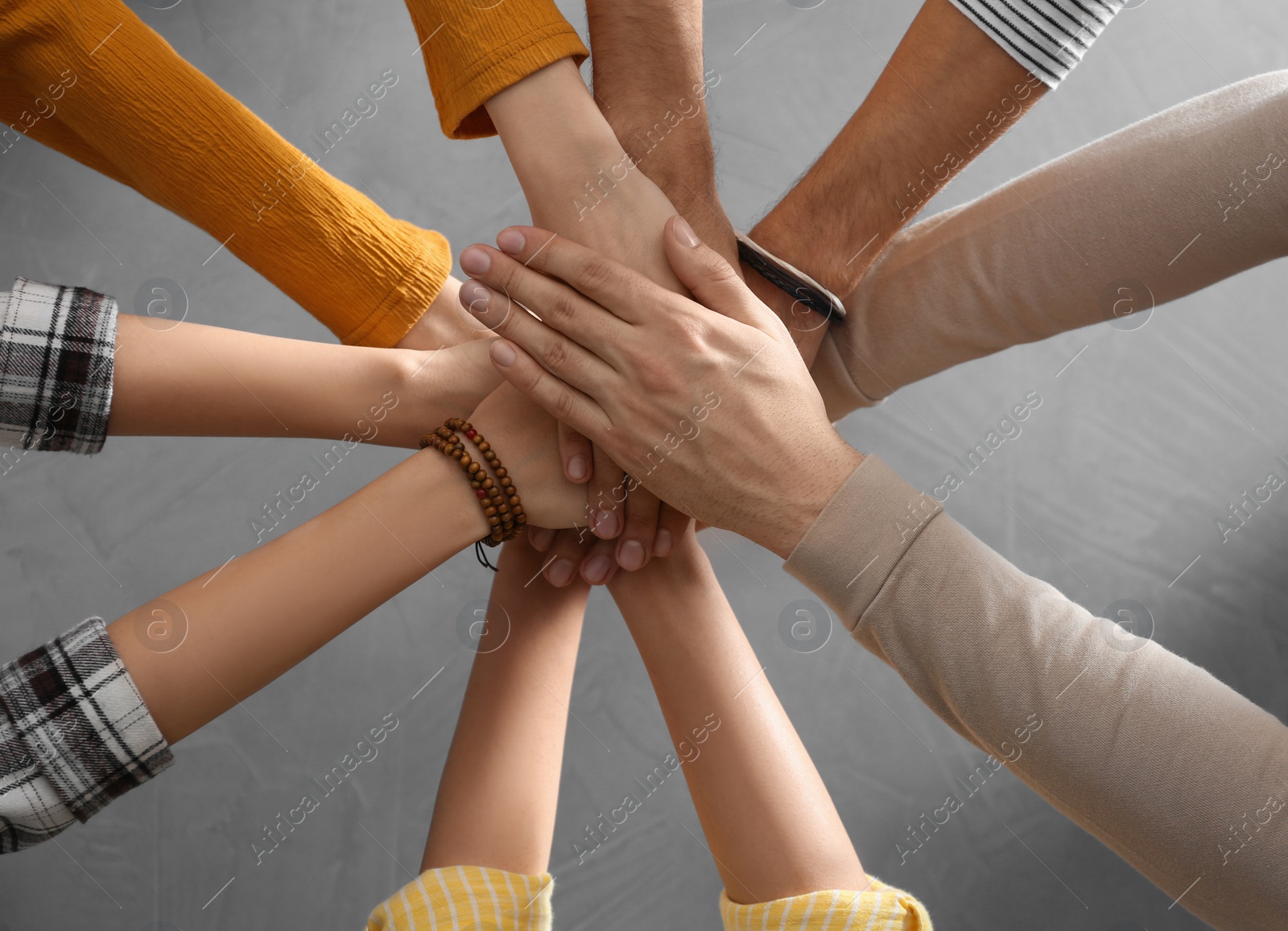 Photo of People holding hands together over grey stone background, top view. Unity concept