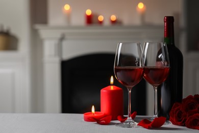 Photo of Glasses of red wine, burning candles and rose flowers on grey table indoors, space for text. Romantic atmosphere