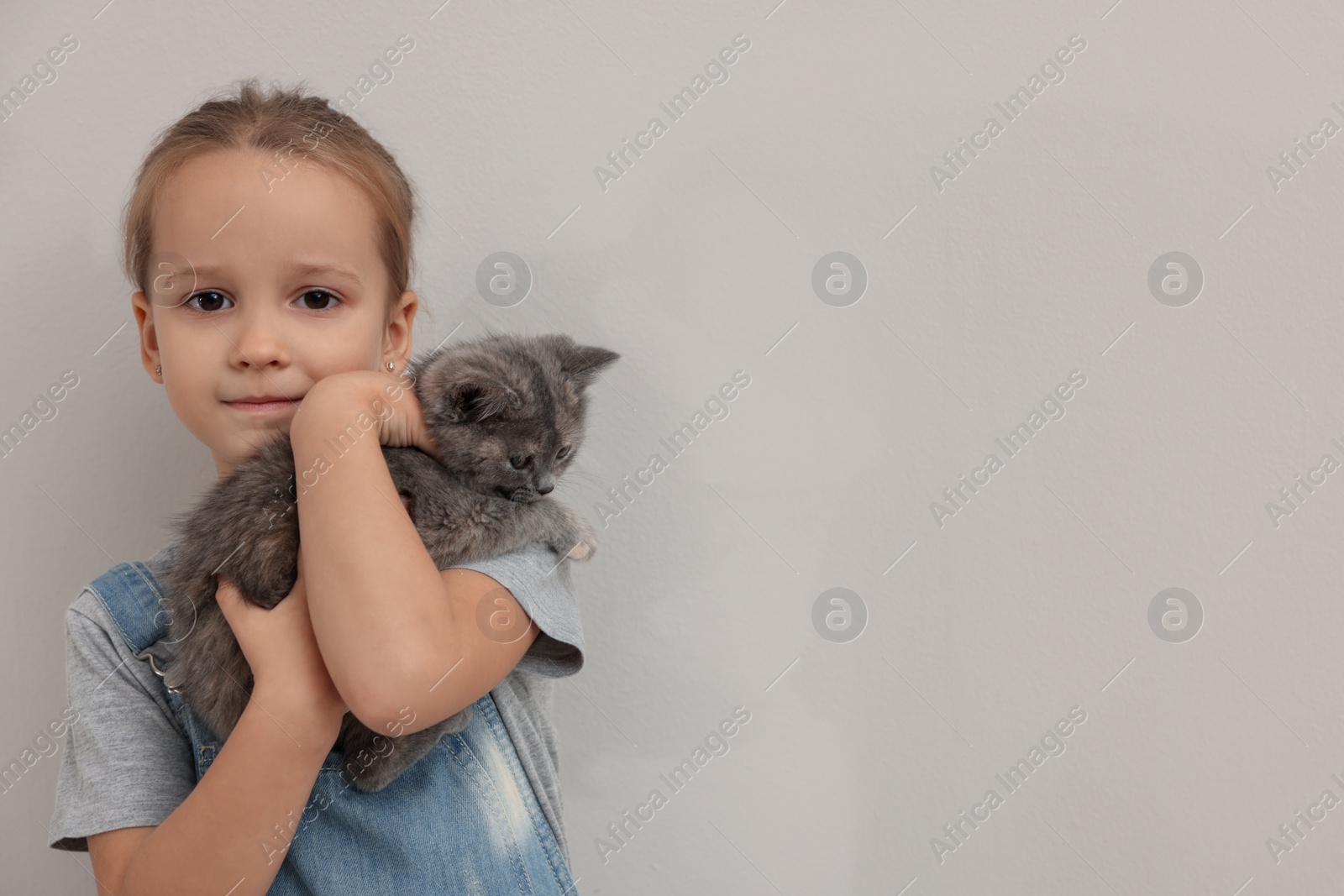 Photo of Cute little girl with kitten on light background, space for text. Childhood pet