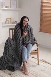 Photo of Young woman with chunky knit blanket in armchair at home