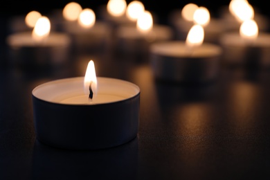 Burning candle on table in darkness, closeup with space for text. Funeral symbol