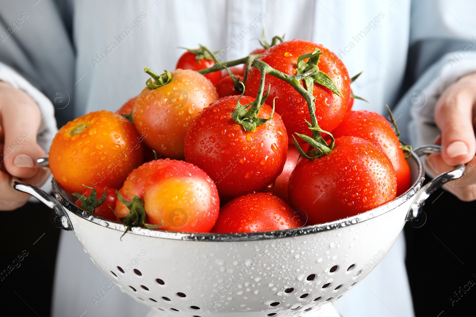 Photo of Woman holding colander with fresh ripe tomatoes on black background, closeup