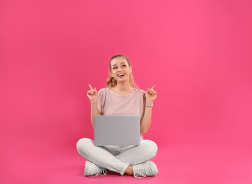 Beautiful young woman with laptop on pink background