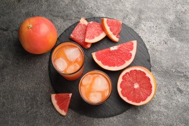 Tasty grapefruit drink with ice in glasses and fresh fruits on dark textured table, flat lay