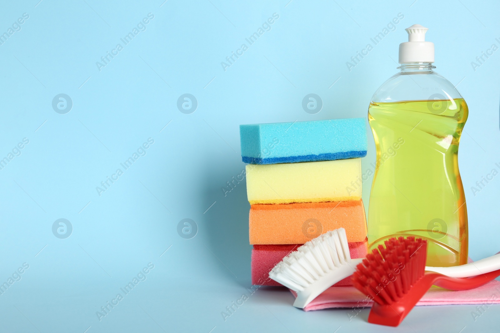 Photo of Cleaning product and tools on light blue background, space for text. Dish washing supplies