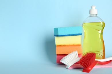 Photo of Cleaning product and tools on light blue background, space for text. Dish washing supplies