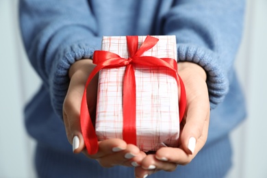 Woman in warm sweater holding Christmas gift on light background, closeup