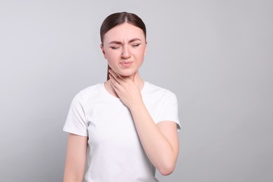 Young woman with sore throat on light grey background