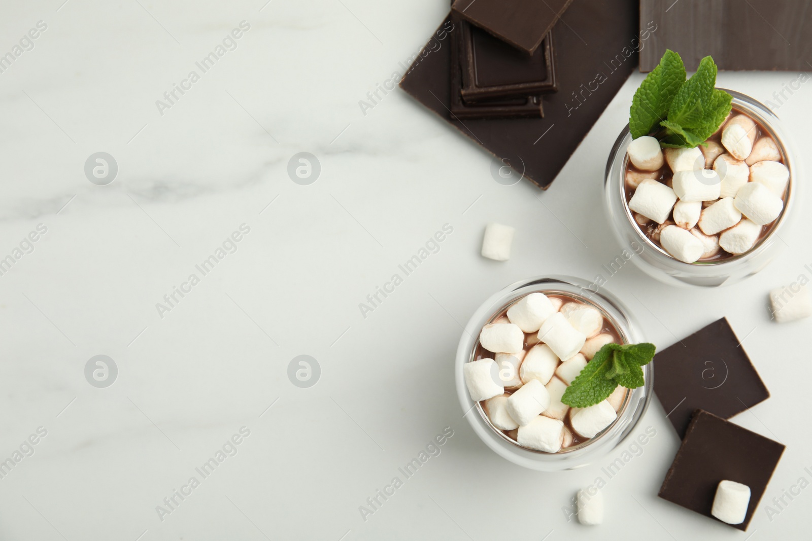 Photo of Glasses of delicious hot chocolate with marshmallows and fresh mint on white marble table, flat lay. Space for text