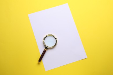 Photo of Magnifying glass and sheet of paper on yellow background, top view
