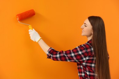 Photo of Happy designer painting orange wall with roller