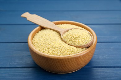 Bowl and spoon with raw couscous on blue wooden table, closeup
