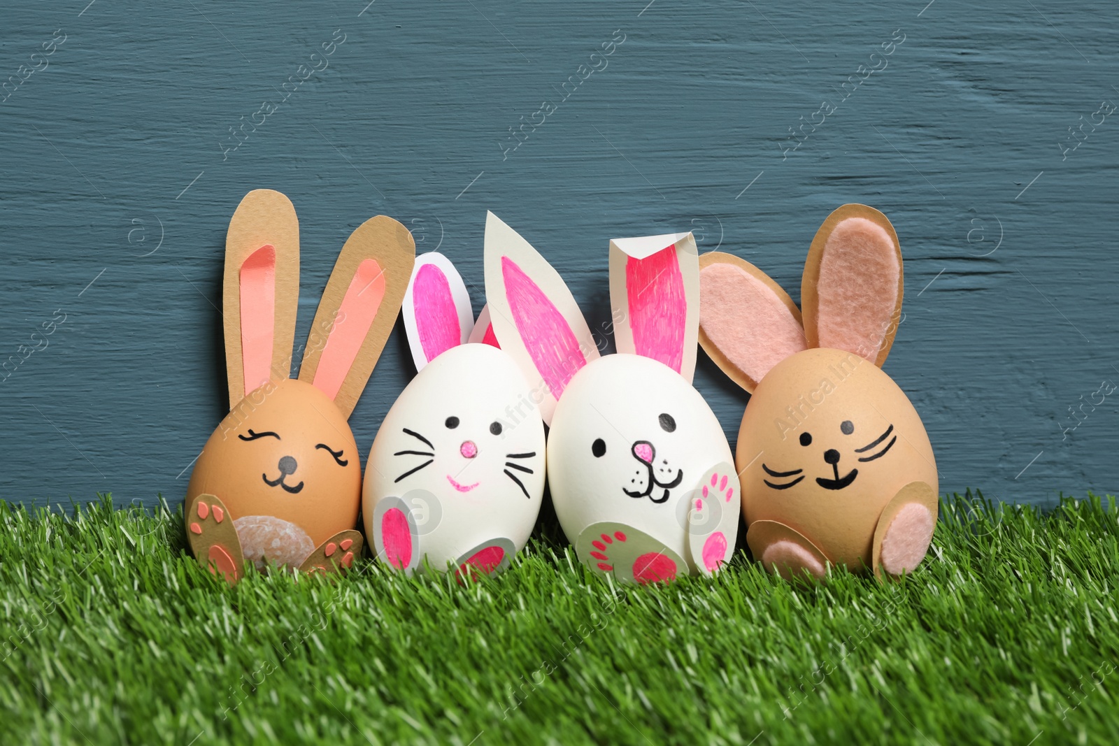 Photo of Easter eggs as cute bunnies on green grass against blue wooden background