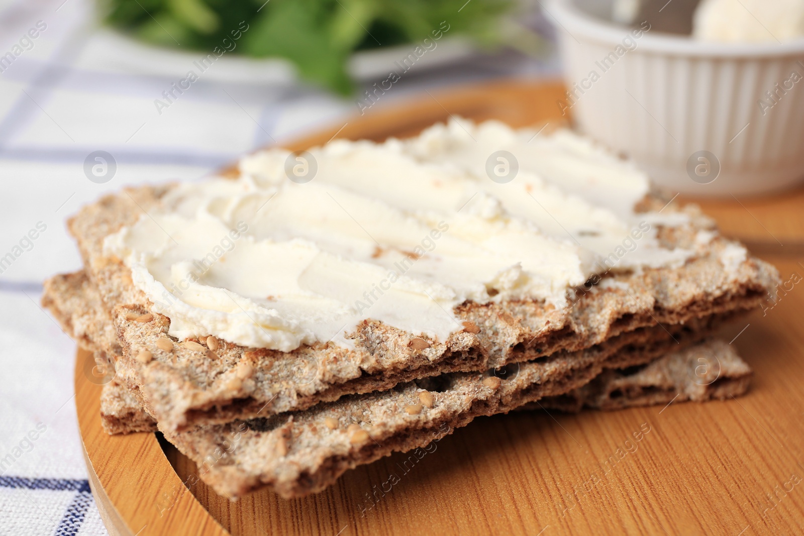 Photo of Fresh crunchy crispbreads with cream cheese on wooden board, closeup