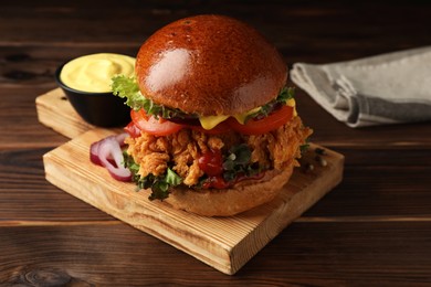 Photo of Delicious burger with crispy chicken patty and sauce on wooden table