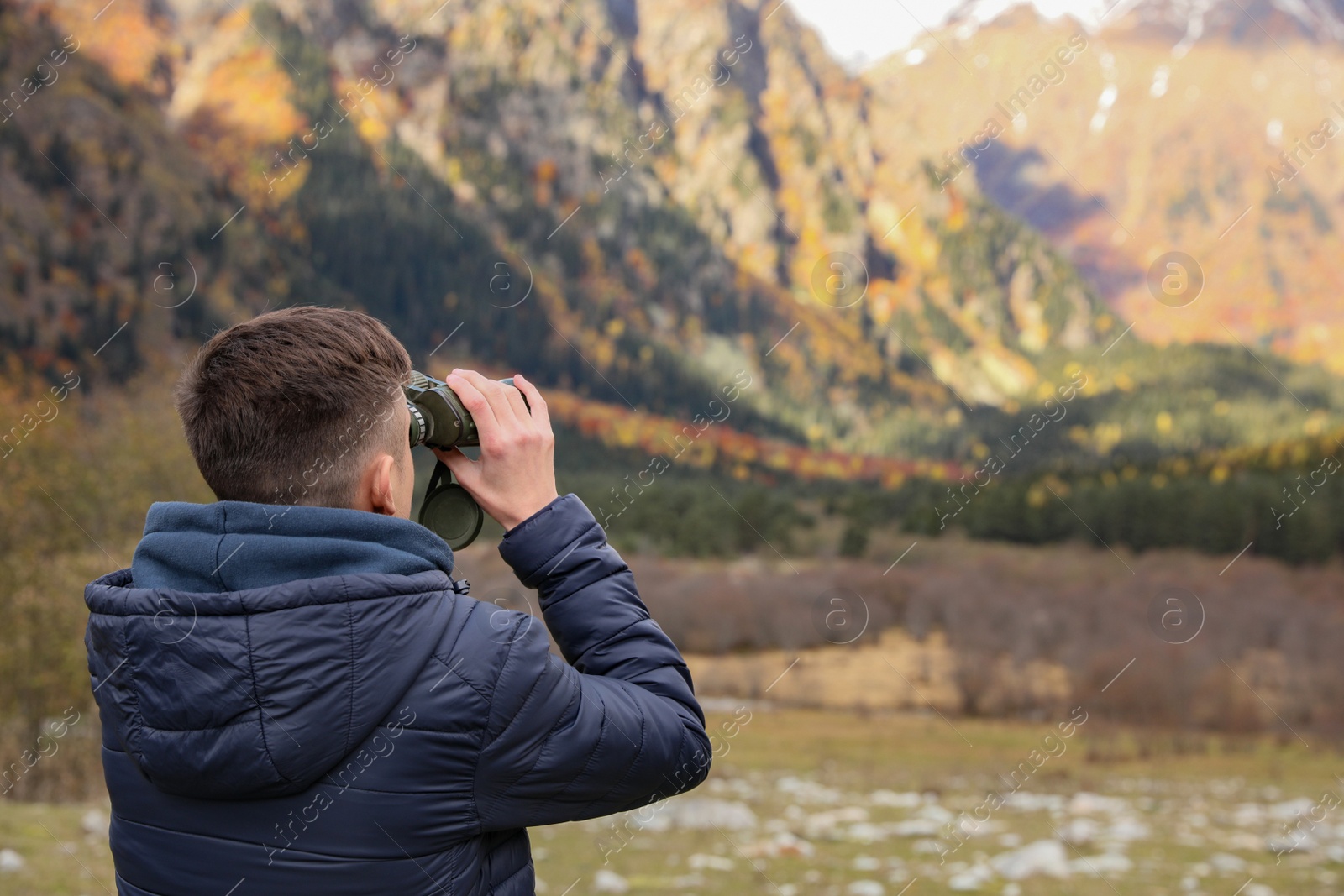 Photo of Boy looking through binoculars in beautiful mountains, back view. Space for text