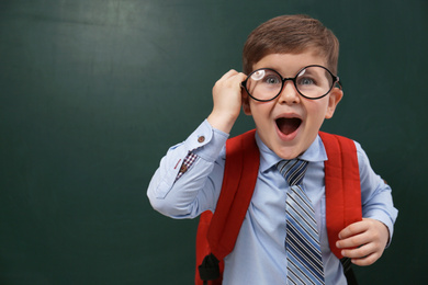 Funny little child wearing glasses near chalkboard, space for text. First time at school