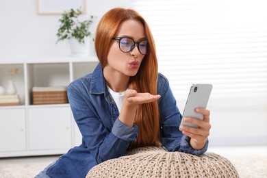 Photo of Happy young woman blowing kiss during video chat via smartphone at home. Long-distance relationship
