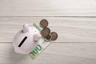 Ceramic piggy bank, coins and euro banknote on white wooden table, flat lay with space for text. Financial savings