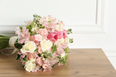 Photo of Beautiful bouquet of fresh flowers on wooden table near white wall