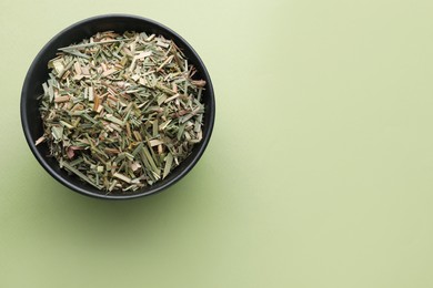 Photo of Bowl with aromatic dried lemongrass on light green background, top view. Space for text