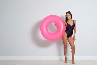 Beautiful young woman with bright inflatable ring near light wall, space for text