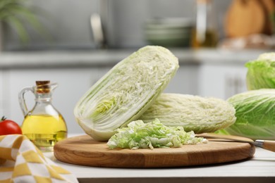 Photo of Fresh Chinese cabbages, knife and oil on white wooden table in kitchen