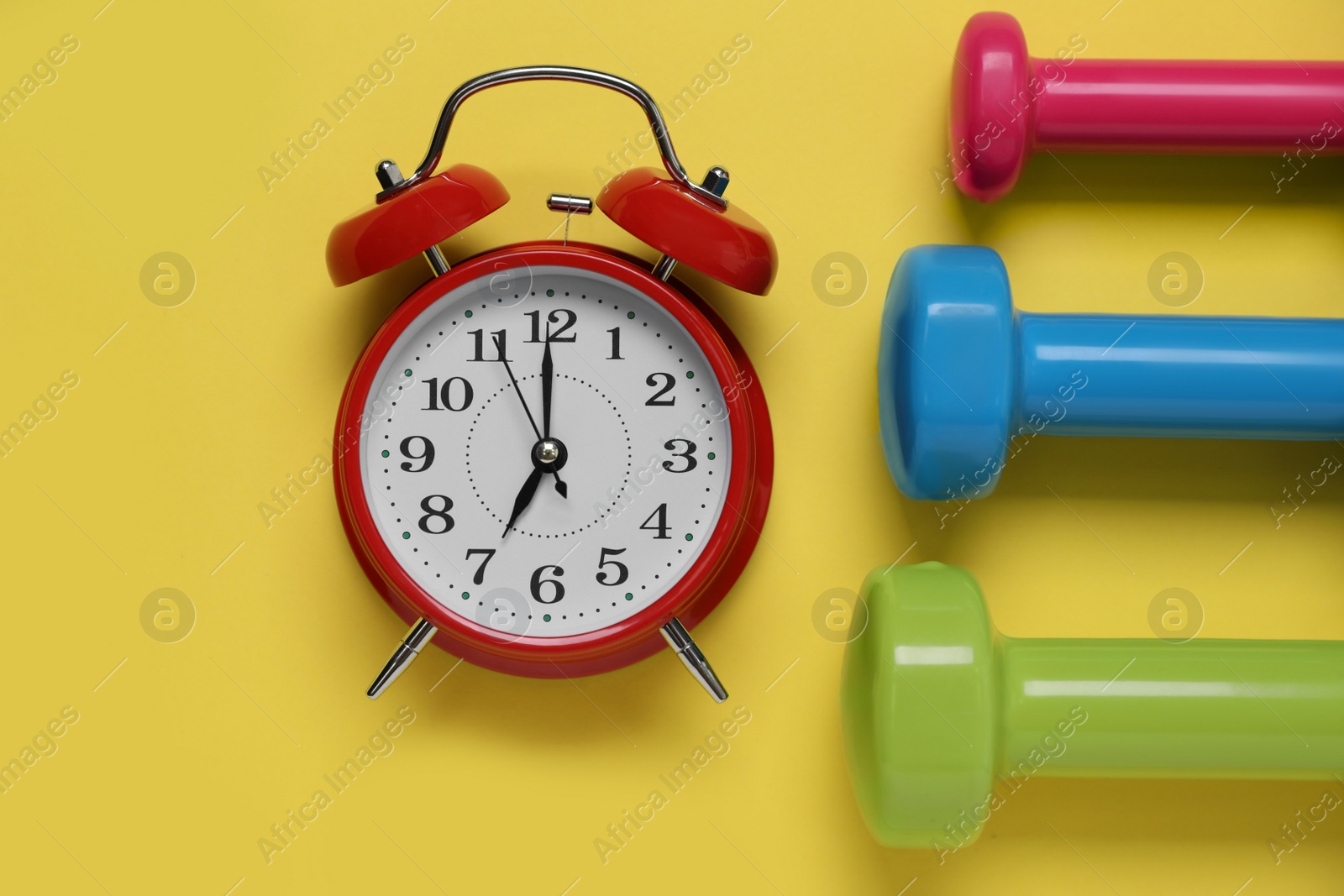 Photo of Alarm clock and dumbbells on yellow background, flat lay. Morning exercise