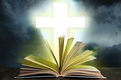 Silhouette of cross and open Bible on grey table against cloudy sky