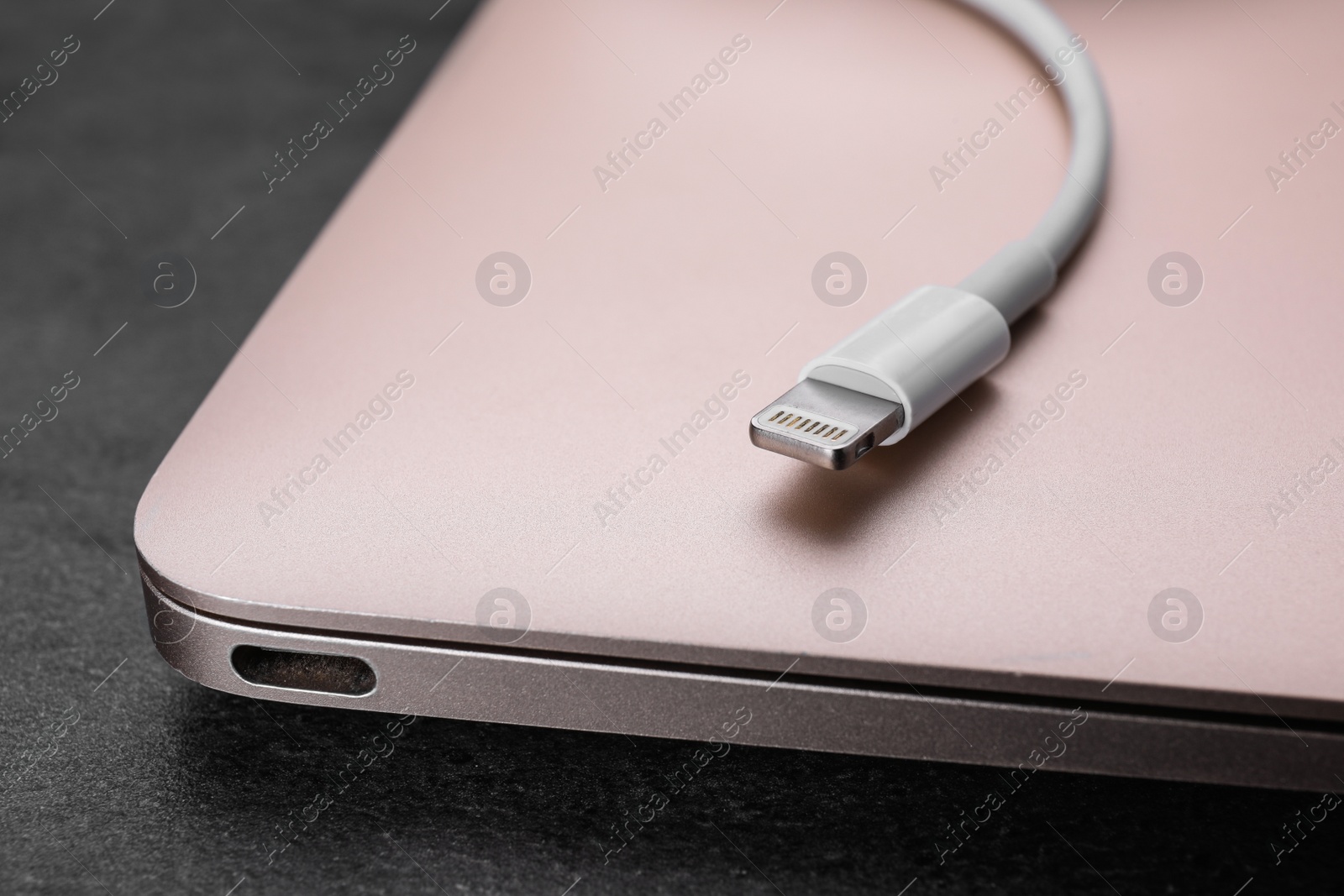 Photo of USB cable with lightning connector and laptop on black table, closeup