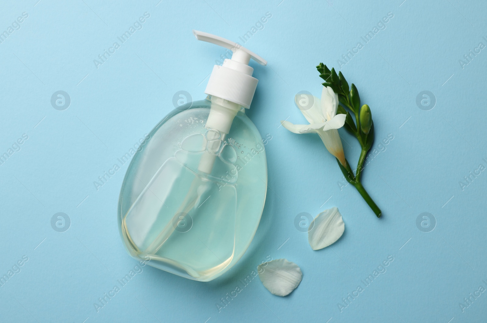 Photo of Bottle of liquid soap and flower on light blue background, flat lay