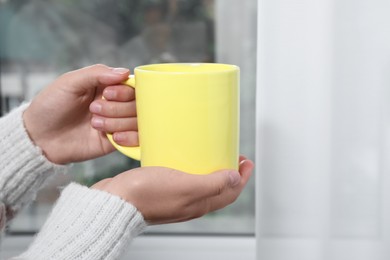 Photo of Woman holding yellow mug indoors, closeup. Mockup for design