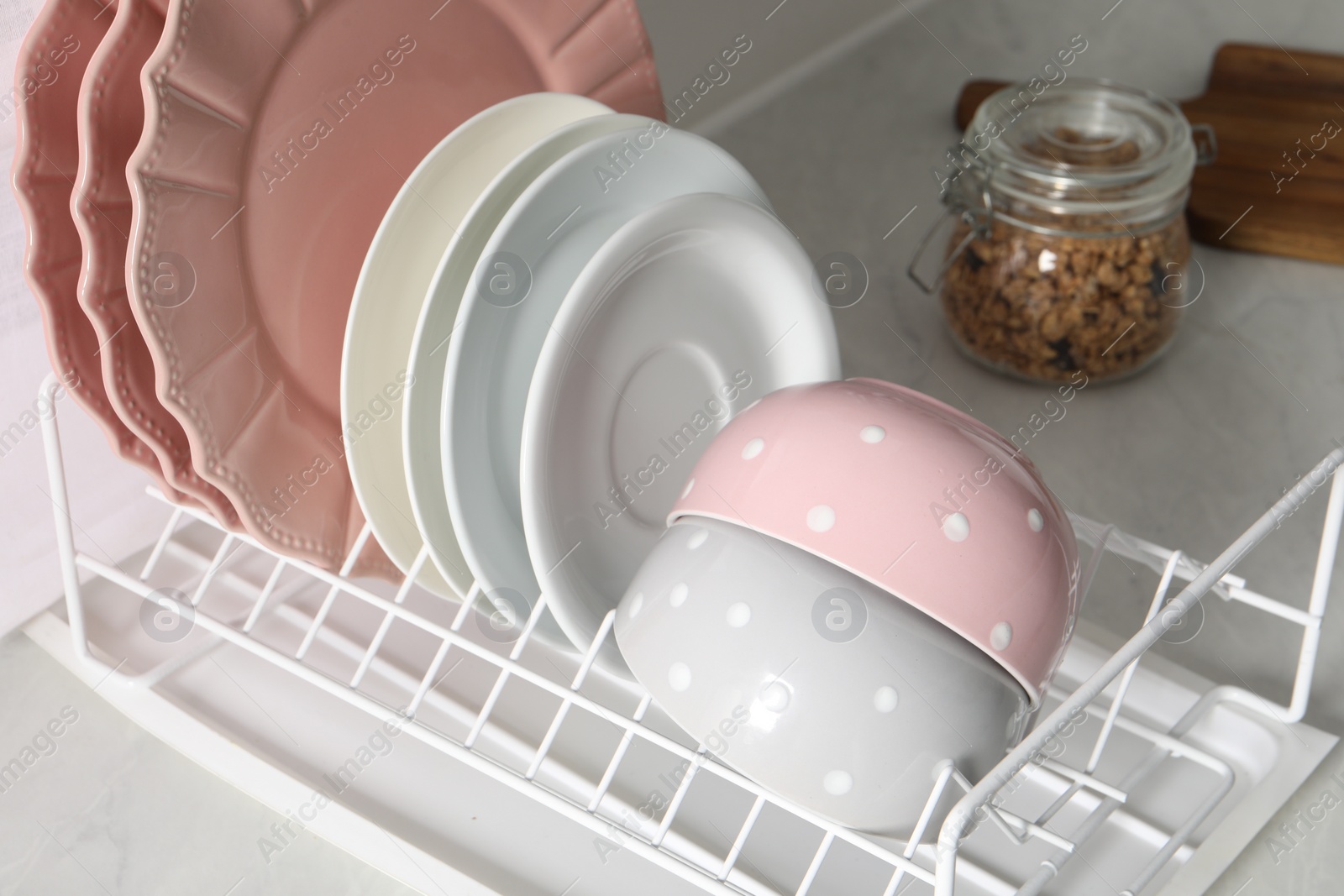 Photo of Drainer with different clean dishware on white table in kitchen