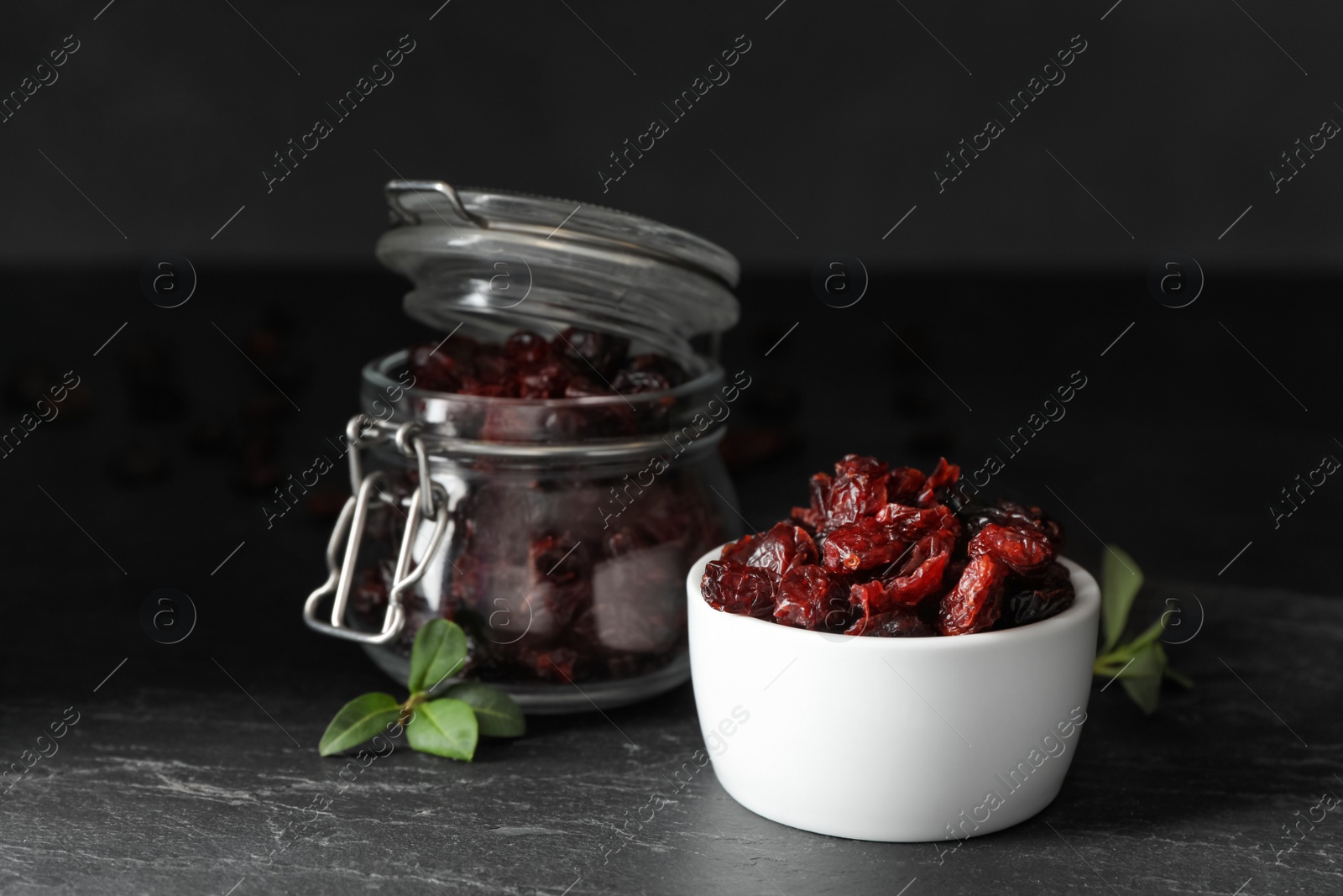 Photo of Tasty dried cranberries and leaves on black table