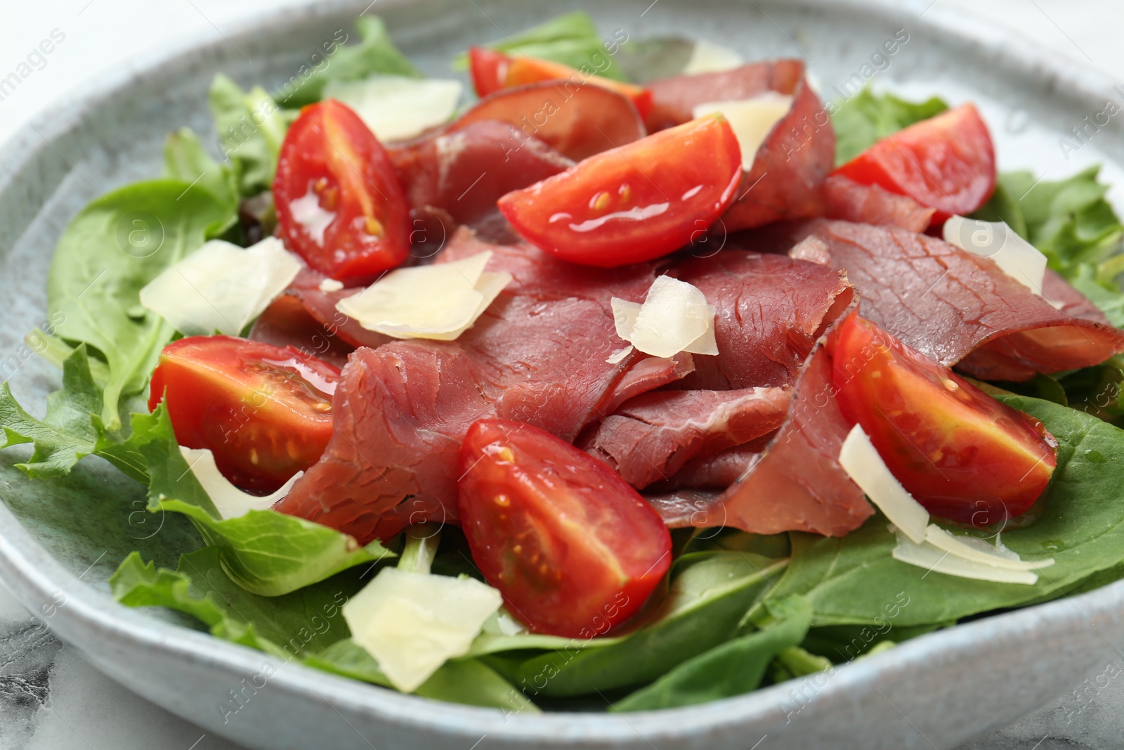 Photo of Delicious bresaola salad with tomatoes and parmesan cheese on table, closeup