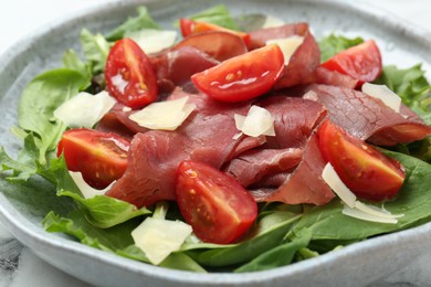 Photo of Delicious bresaola salad with tomatoes and parmesan cheese on table, closeup