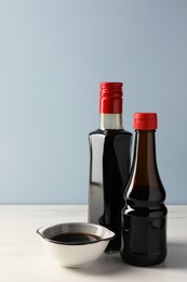 Photo of Bottles and bowl with soy sauce on white table