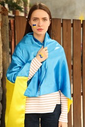 Young woman with Ukrainian flag near wooden fence outdoors