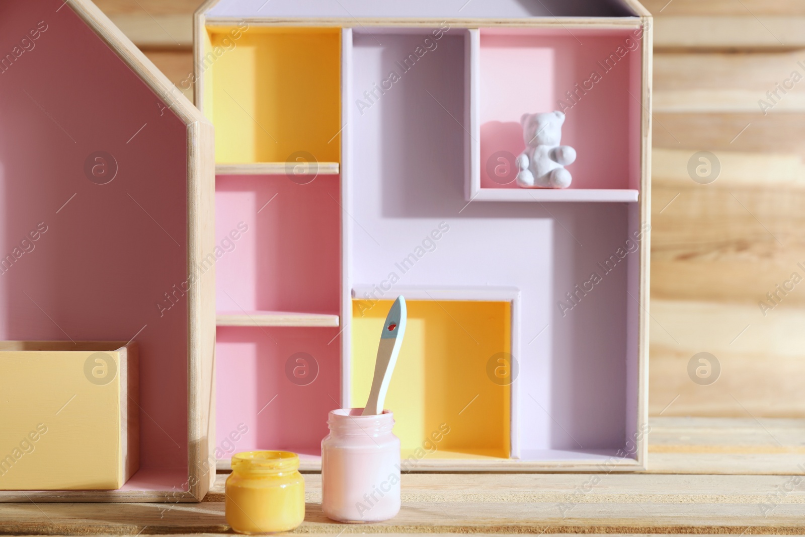 Photo of House shaped shelves, jars of paints and brush on wooden table. Interior elements