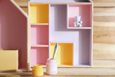 Photo of House shaped shelves, jars of paints and brush on wooden table. Interior elements