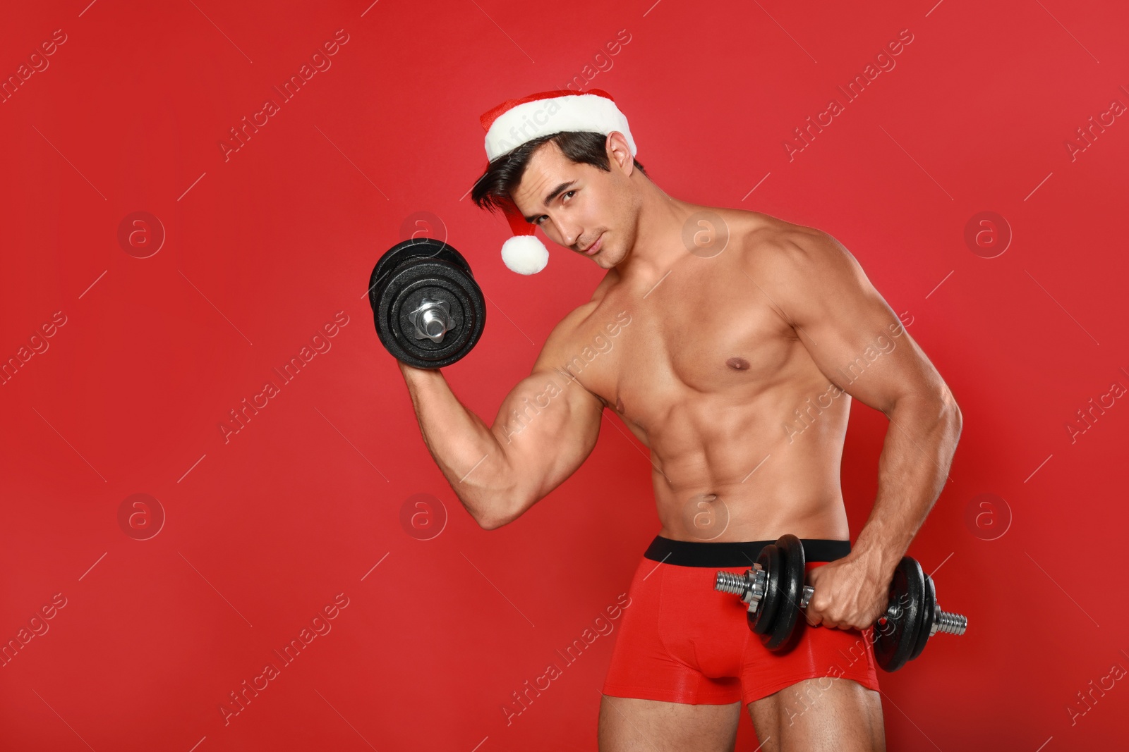 Photo of Sexy shirtless Santa Claus with dumbbells on red background