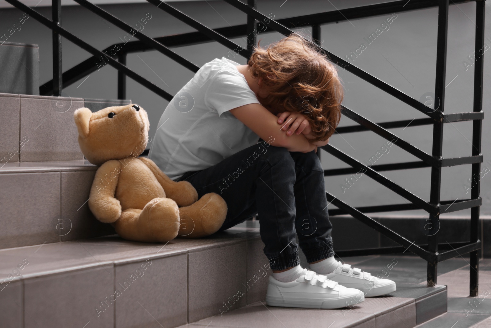 Photo of Child abuse. Upset boy with toy sitting on stairs