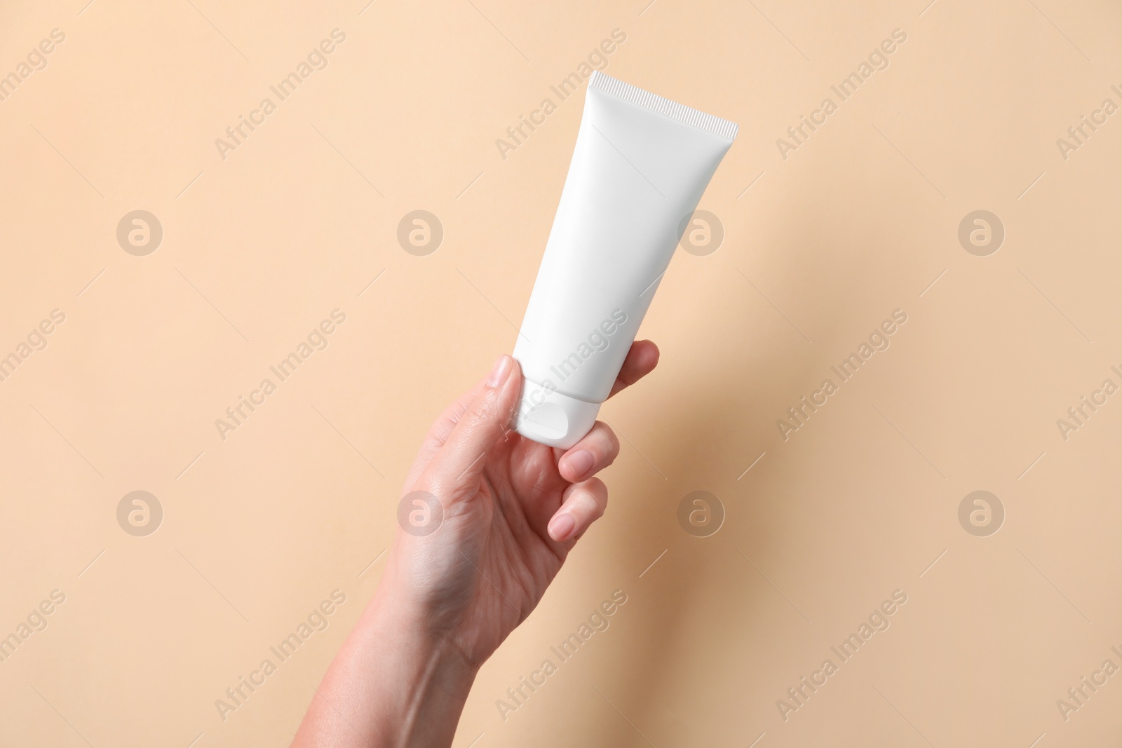 Photo of Woman with tube of hand cream on beige background, closeup