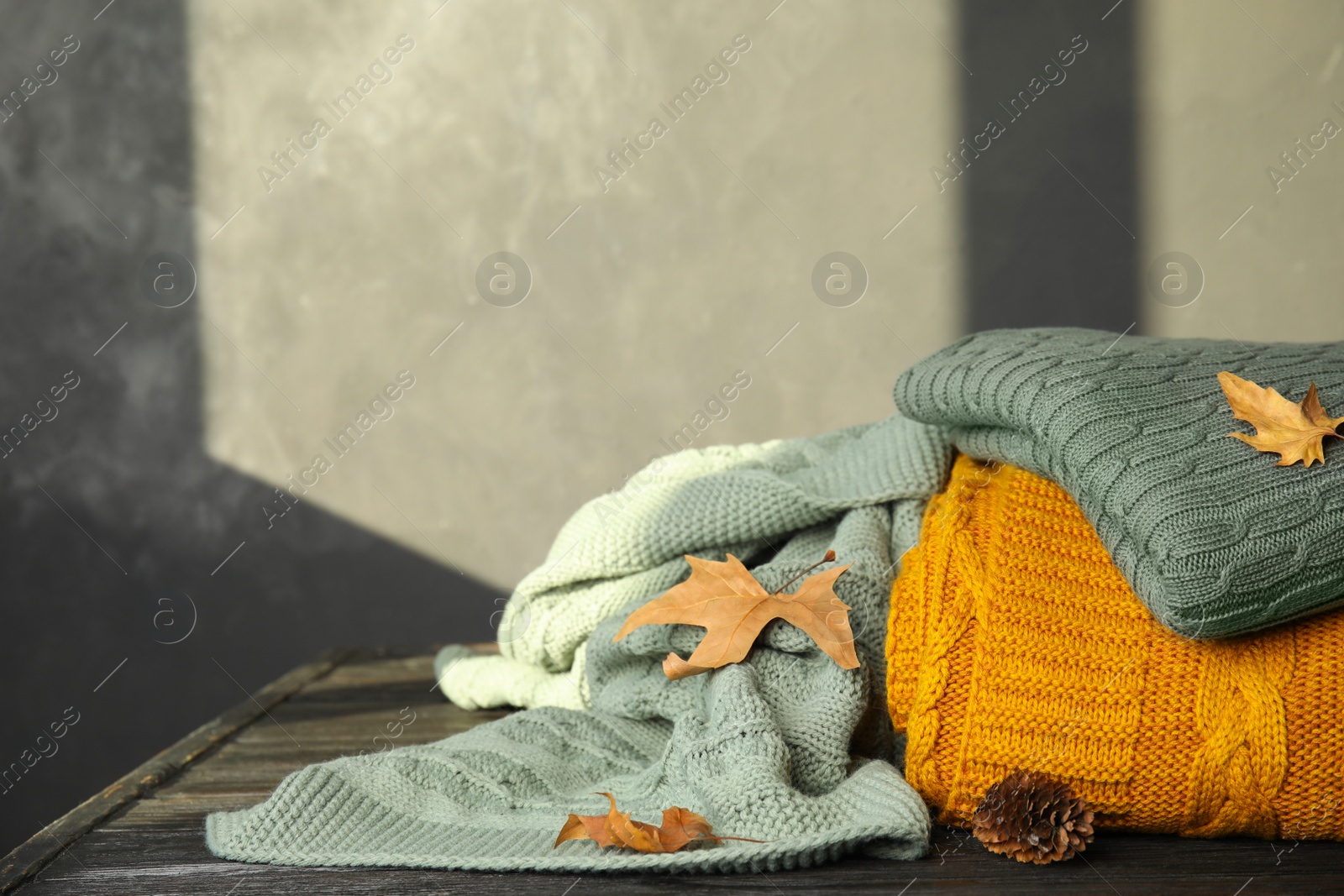 Photo of Different soft plaids, dry leaves and fir cone on black wooden table. Space for text