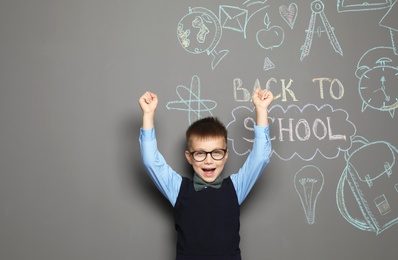 Little child in uniform near drawings with text BACK TO SCHOOL on grey background