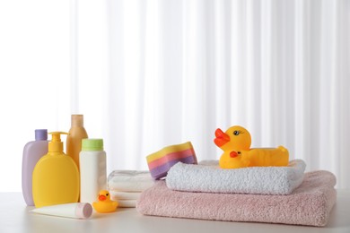 Towels, rubber ducks and baby care products on white table indoors