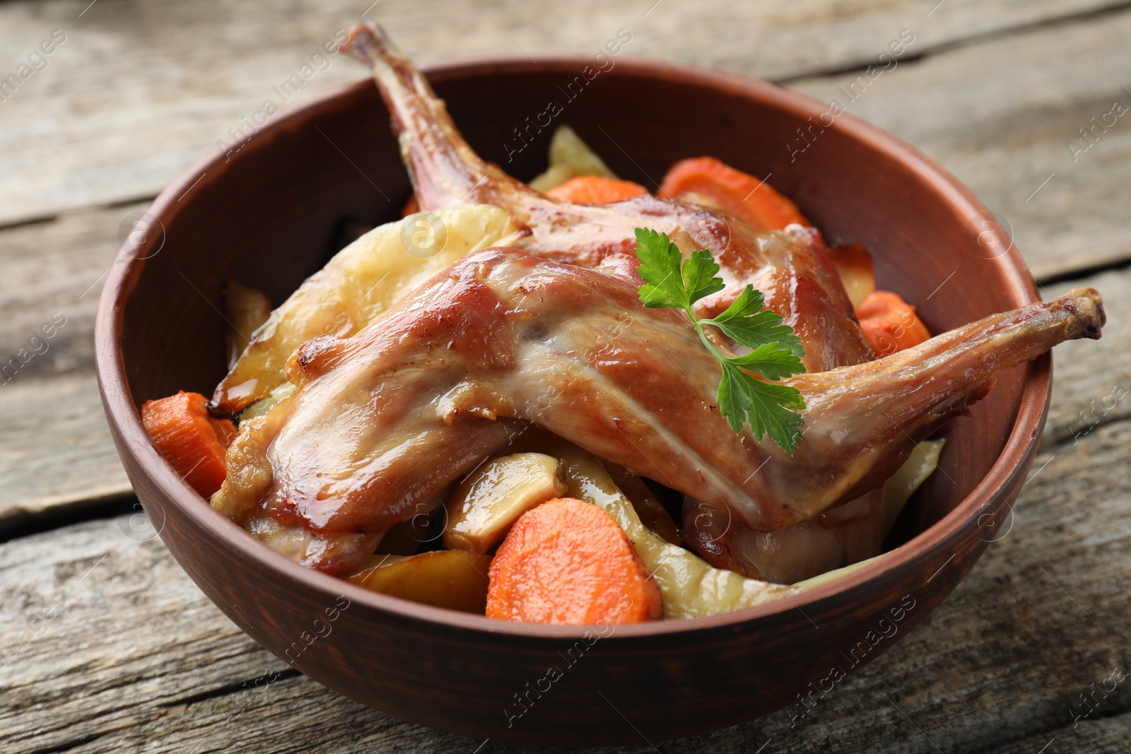 Photo of Tasty cooked rabbit with vegetables in bowl on wooden table, closeup